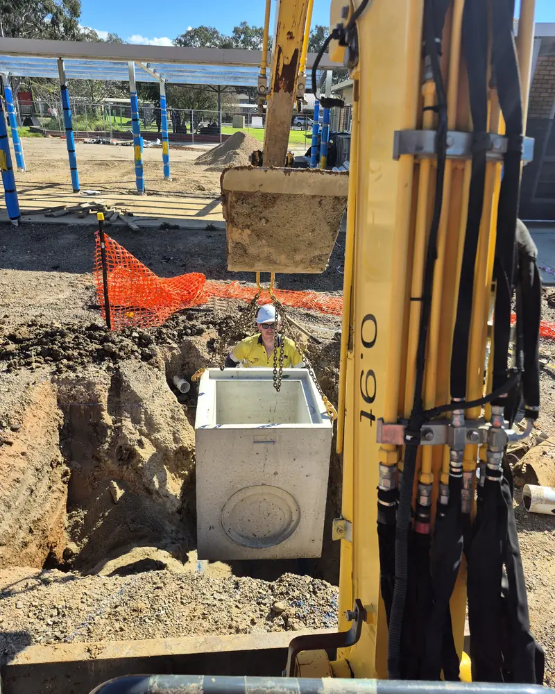 Excavator lowering a precast concrete pit into position